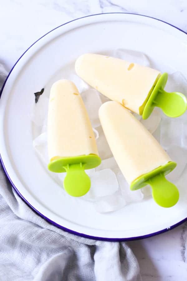 3 mango popsicles on a bed of ice cubes.