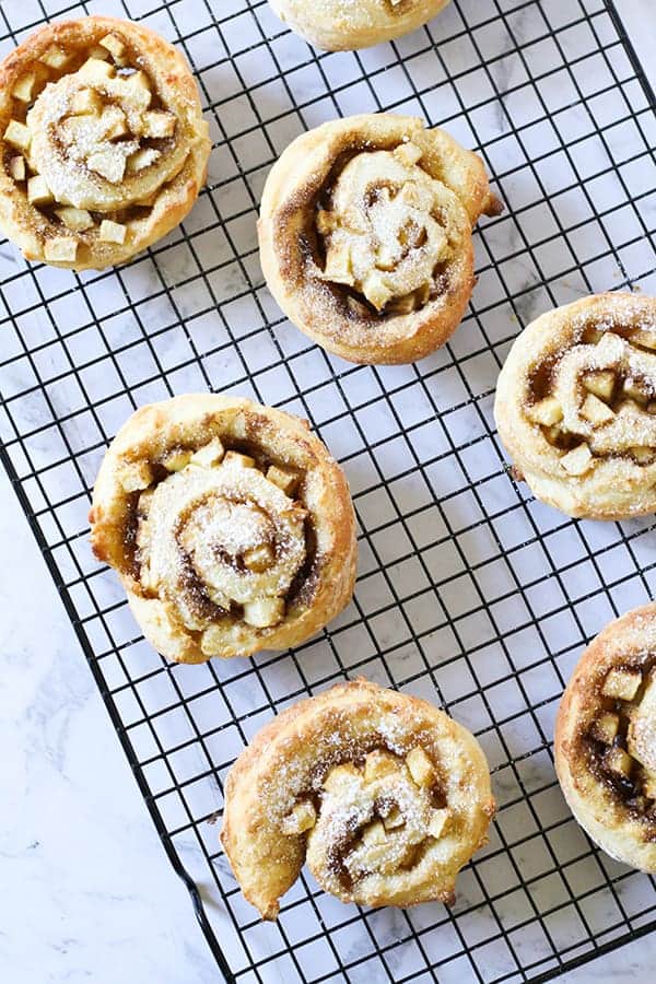 apple and cinnamon scrolls sitting on a cooling rack.