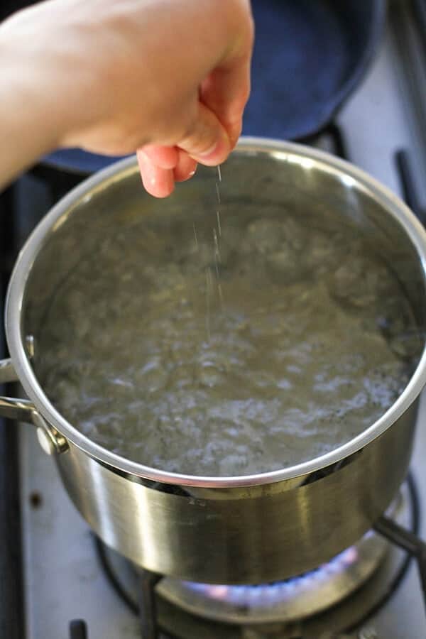 Hand sprinkling salt into a saucepan of boiling water.