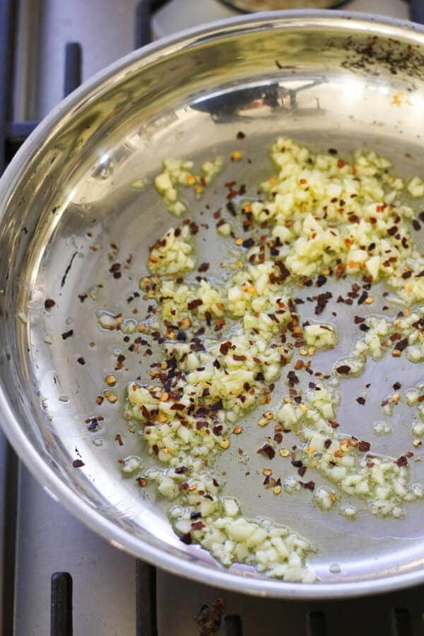 garlic and red pepper flakes sautéing in a frying pan.