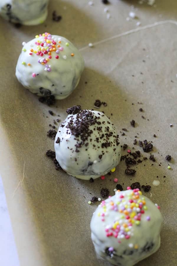 oreo balls laying on baking tray covered in cookie crumbs and sprinkles.