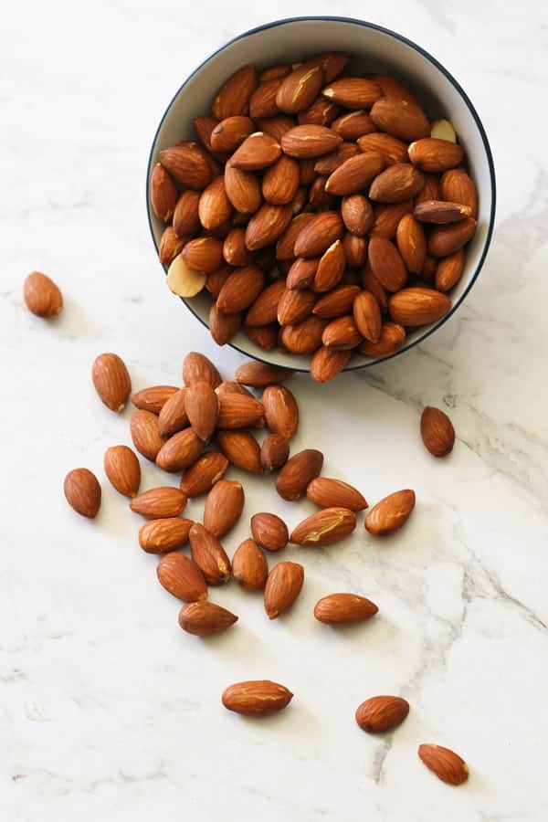 Dry roasted almonds in a small bowl and on a white marble bench.