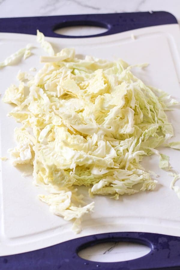 shredded cabbage on a white cutting board.