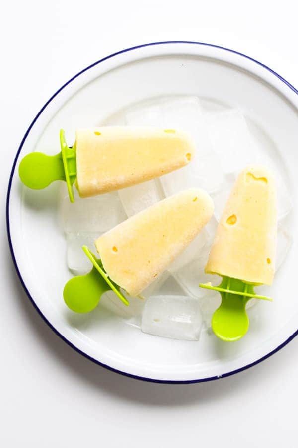 mango pineapple popsicles on a white plate covered in ice cubes.