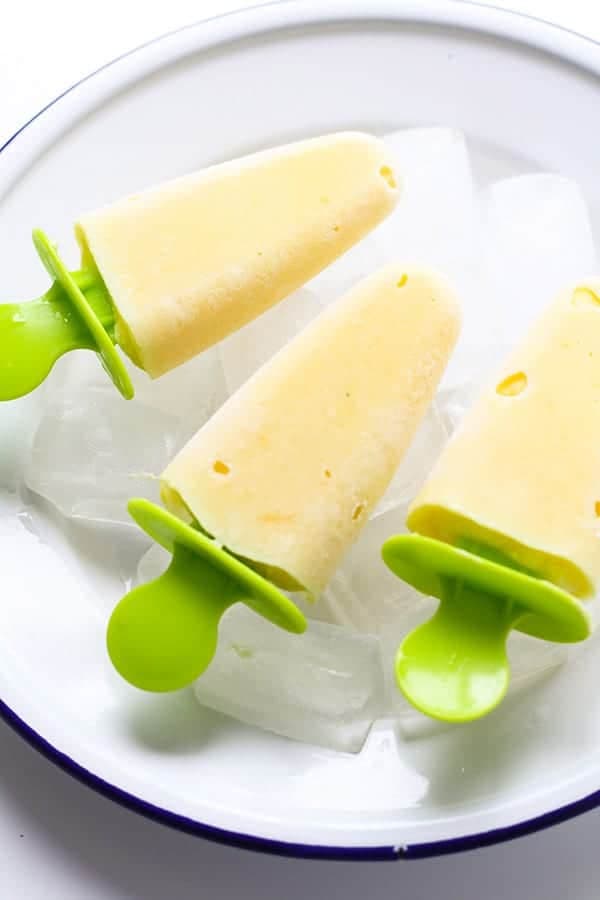 mango pineapple popsicles on a white plate covered in ice cubes.