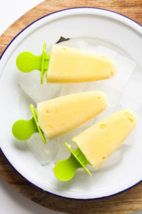 mango pineapple popsicles on a white plate covered in ice cubes.