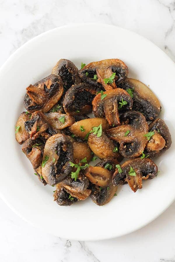 mushrooms on a white plate with parsley sprinkled over.