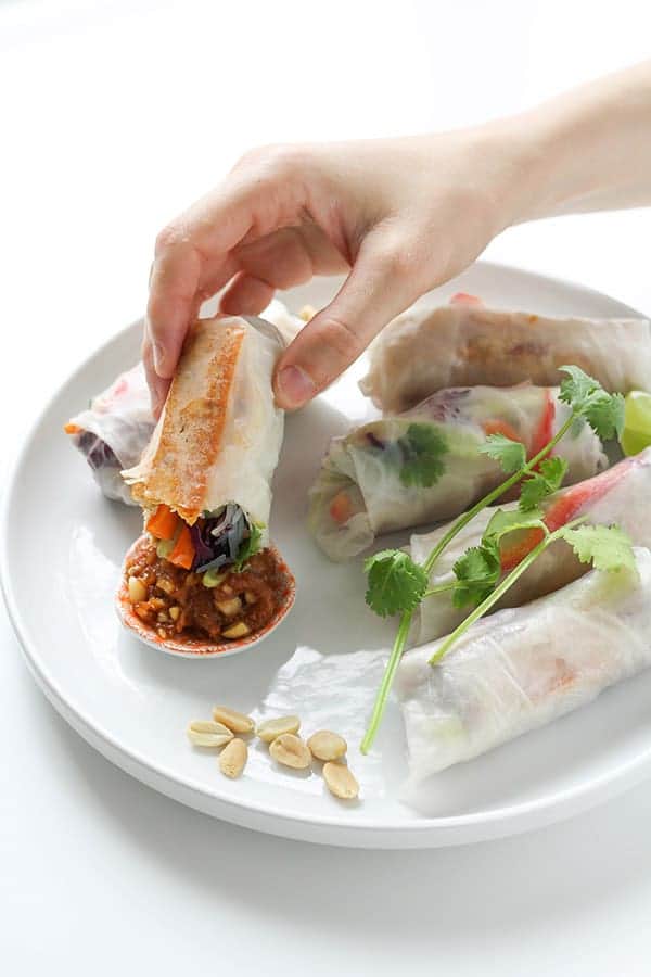 a hand dipping a rice paper roll into a peanut sauce.