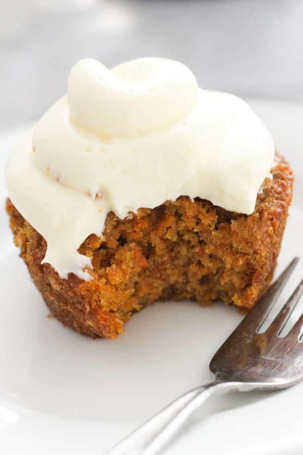 carrot cupcake on a white plate with a bite removed.