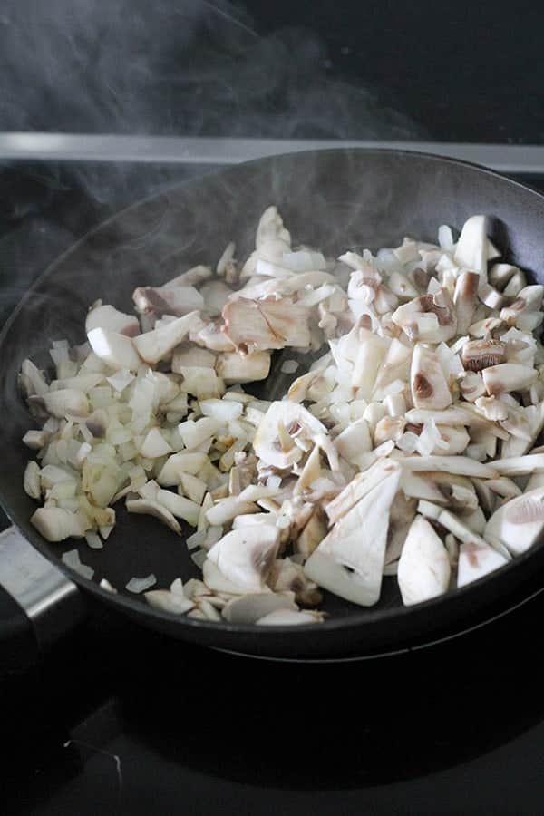onion and mushroom being sautéed in a frying pan.