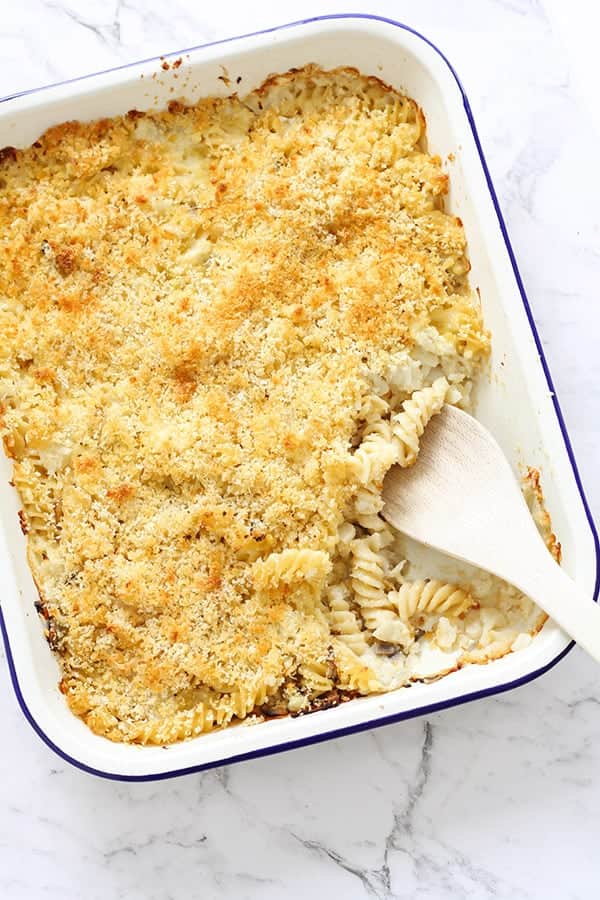 creamy vegetable pasta bake in a white baking dish with a wooden serving spoon.