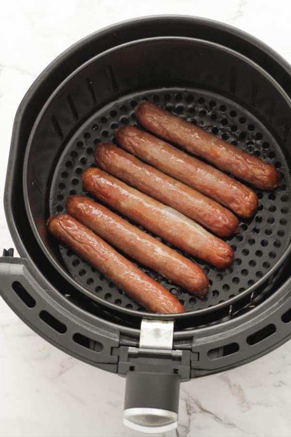 cooked sausages in an air fryer basket.
