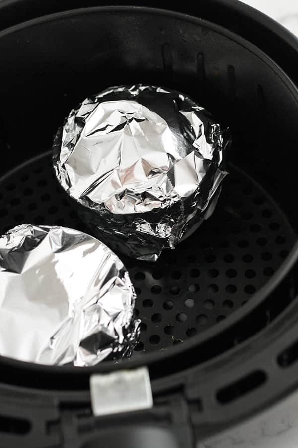 ramekins covered in foil in an air fryer basket.