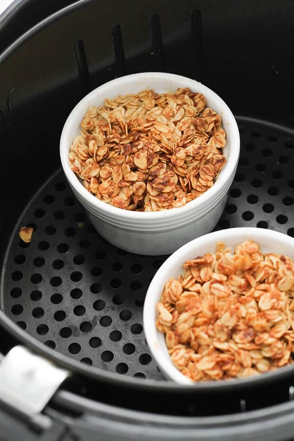 two ramekins filled with apple crisp in an air fryer basket.
