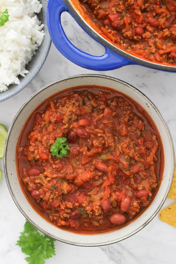 a bowl of chilli, a bowl of rice and a large pot of chilli sitting on a counter top.