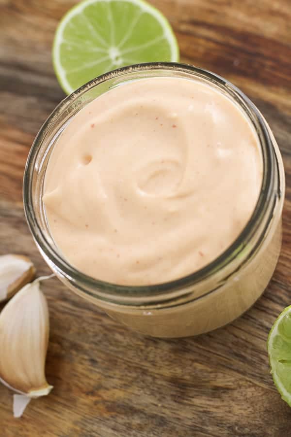 sriracha aioli in a glass jar on a wooden serving platter.