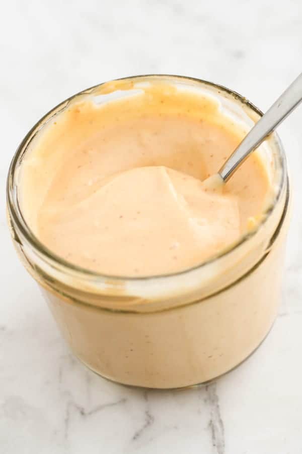 sriracha aioli in a glass jar with a spoon stuck inside.