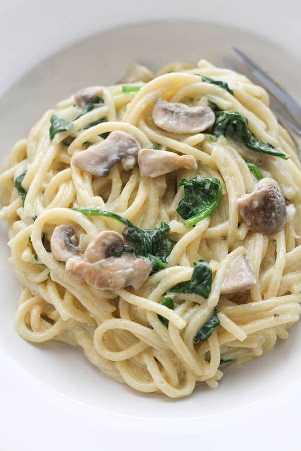 spinach and mushroom pasta in a white bowl.