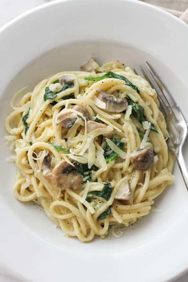 creamy spinach and mushroom pasta in a white bowl.