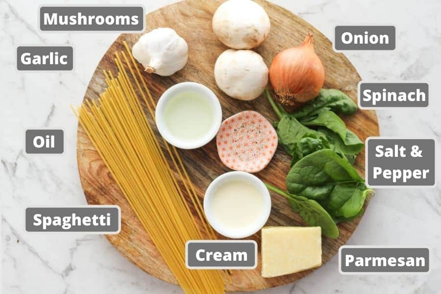 ingredients for spinach and mushroom pasta on a wooden board.