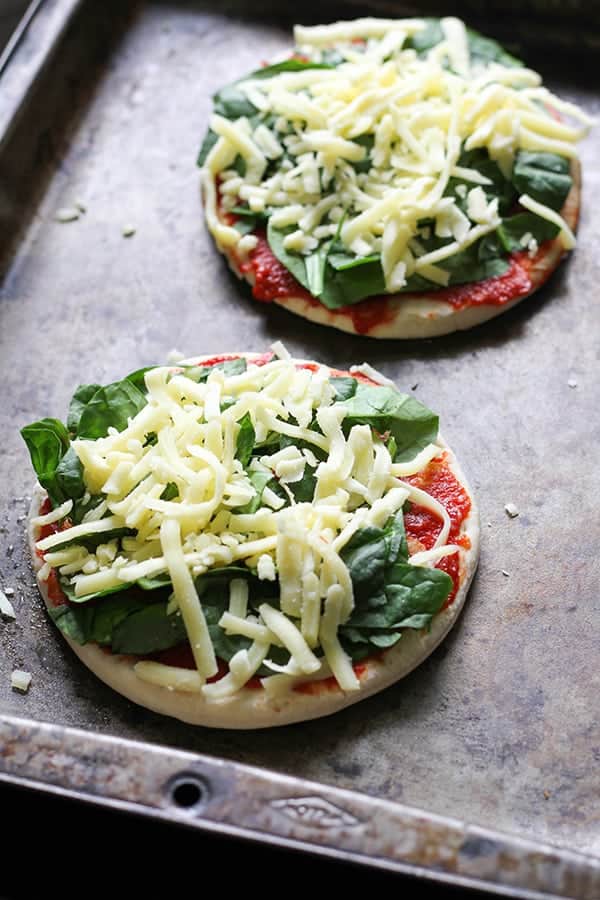 pizza bases on a baking tray covered with spinach and cheese.