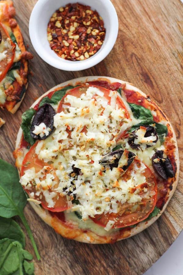 pizza topped with halloumi, spinach and tomato on a wooden serving board.