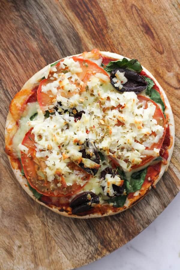 pizza topped with tomato, spinach and halloumi cheese on a wooden board.