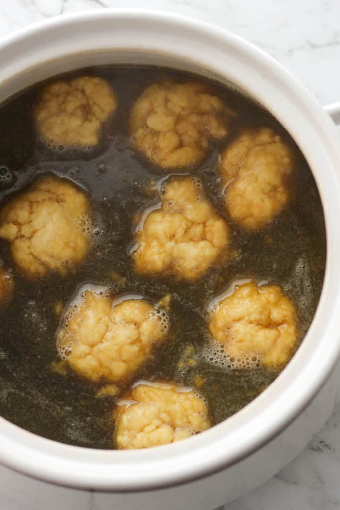 dumplings floating in caramel sauce in a baking dish.