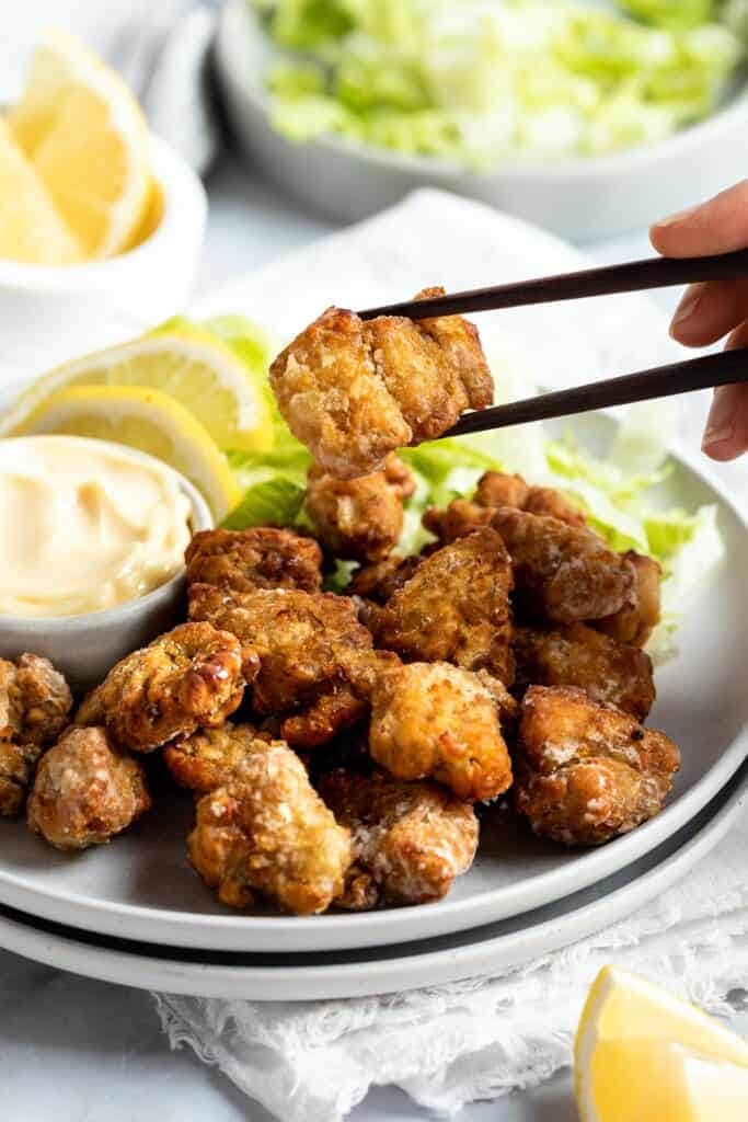a chopstick holding a piece of karaage chicken in the air above a plate of karaage.